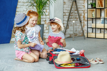 Three happy children pack their clothes in a suitcase. Concept, lifestyle, childhood, trip, vacation, family, tourism.