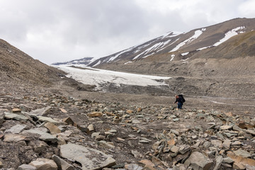 Man searching for fossils in a rocky Longyear glacier moraine in Svalbard, Norway. The glacier edge in the background.