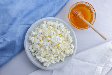 Fresh cottage cheese with honey on a white background, soft cheese with a blue napkin, dairy product with honey, healthy food, French breakfast, American cuisine, minimalism, curd with goat milk