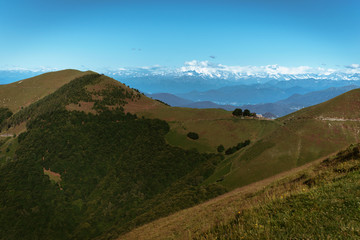 Panoramic View of beautiful landscape in the Italian Alps with fresh green meadows and snow-capped mountain tops in the background on a sunny day with blue sky and clouds in springtime.