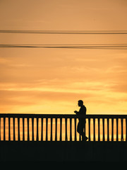 Silhouette of man walking on the bridge with cigarettes on sunset.