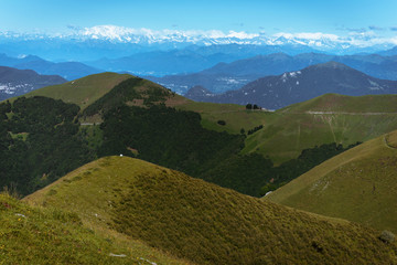 Obraz premium Panoramic View of beautiful landscape in the Italian Alps with fresh green meadows and snow-capped mountain tops in the background on a sunny day with blue sky and clouds in springtime.