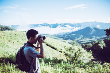 Young man is photographing autumn landscape in fog at sunrise