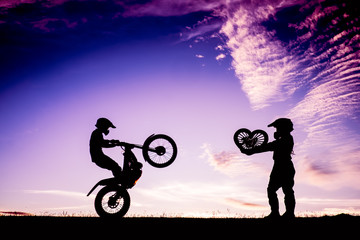 Silhouette of Couple standing and heart shape in handwith a motorcycle in the sunset, Happiness and joy dating couples.