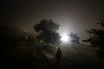 Strange silhouette in a dark spooky forest at night, mystical landscape surreal lights with creepy man