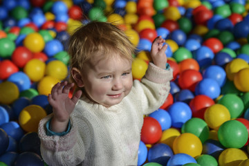 happy little child plays on a playground filled with colorful plastic balls.