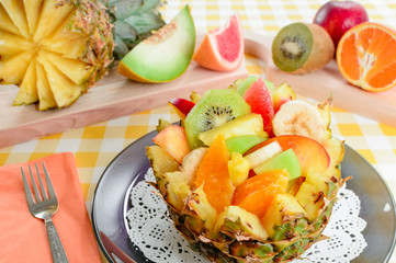 Fresh fruit salad with kiwi, banana, peach, orange, red orange, apricot and melon in handmade pineapple bowl.