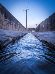A narrow river stream of water flowing through the canal made of cement