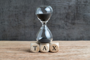 Time countdown for tax deadline concept, hourglass or sandglass on cube wooden block with alphabets...