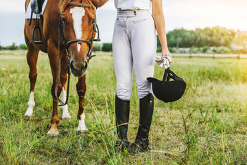 a young jockey girl stands near her horse