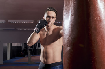 one boxer, punching boxing bag, indoors room. shirtless, wearing boxing gloves.