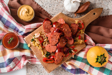 Sliced sausage and mix of fresh vegetables served on a rustic wooden board, mustard, ketchup, fresh hot chili peppers and herbs.