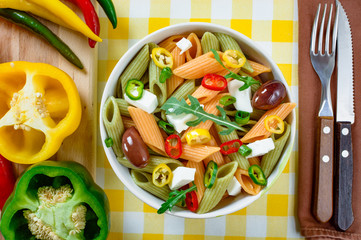 Pasta salad with tomato,arugula, cucumber, peppers,hot peppers, black and green olives, and cheese feta.  Top view.