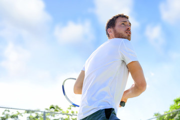 Fototapeta premium Tennis player man playing game hitting ball finishing serve outdoor. Sport fitness athlete outside with tennis racket. Fit young male caucasian professional living healthy active lifestyle.