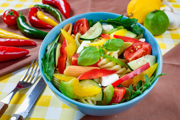 Pasta salad with tomato,arugula, cucumber, peppers,hot peppers, black and green olives, and cheese feta.  Top view.