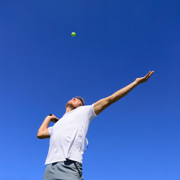 Tennis player man doing serve in position to hit ball in the air. Playing tennis outdoors on blue sky summer background. Active sport athlete doing fitness fun.