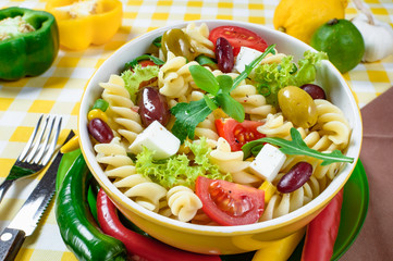 Pasta salad with tomato,arugula, cucumber, peppers,hot peppers, black and green olives, and cheese feta.  Top view.