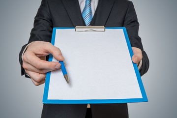 Man is showing and offering blank white paper in clipboard with pen.