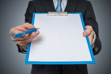 Man is showing and offering blank white paper in clipboard with pen.