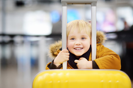 Cute happy little boy with big yellow suitcase at international airport before flight