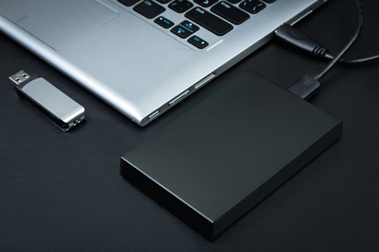 External hdd connected to the laptop and USB flash drive on a black background, top view. The concept of portable data storage