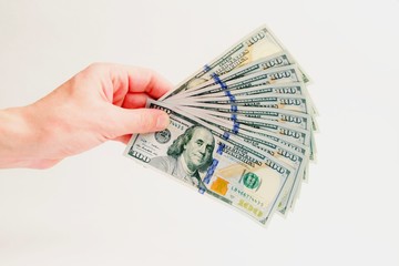 A fan of hundred-dollar bills. A thousand dollars in the left male hand on a white background. How to earn and cash money. Isolated. Close-up.