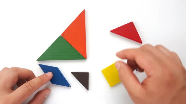 man playting wooden tangram and making it shaped like a sailboat on white