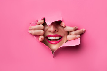 close-up of female fingers, nose and lips with pink lipstick and a broad smile that peeps through the pink grafted paper