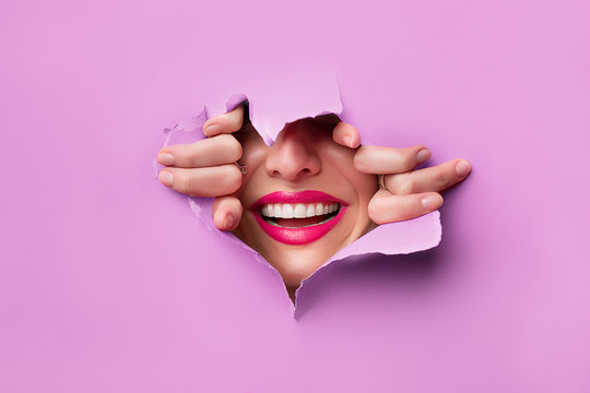 close-up of female fingers, nose and lips with pink lipstick and a broad smile that peeps through purple grapesafed paper