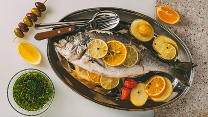 Fototapeta na wymiar Sea gilt-head bream fish on the plate baked with potatoes, rosemary, lemon, orange, olives, tomatoes and lime. Fresh Orata, Dorade fish preparation.
