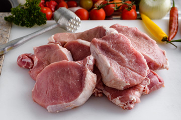 Raw meat, pork steaks on kitchen  table. Vegetables and meat hammer in the background.