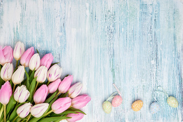 Pink tulips and decorative Easter eggs on blue background. Top view, copy space. Holiday background.