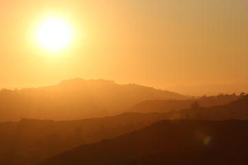 bright yellow sun by a silhouette of layers of mountains
