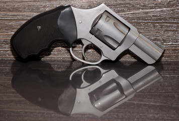 A stainless steel .357 magnum revolver on a reflective surface with a wooden background