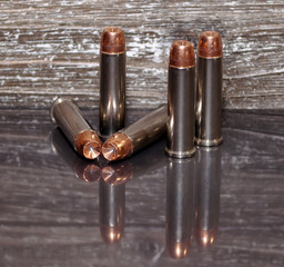 Five .357 magnum bullets with a wooden background and on a reflective surface showing the bullets.