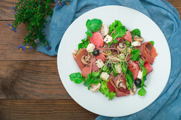 Salad with spinach, cheese, ham, grapefruit and balsamic sauce on a wooden rural background. Top view. Close-up