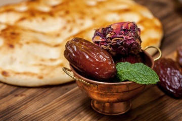 Close up with dates and middle eastern desserts with rose petals in a small copper cup