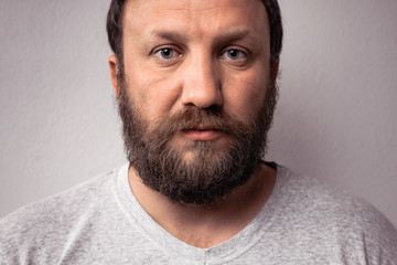 Fototapeta premium Long beard and mustache of handsome bearded man, portrait of bearded man in gray t-shirt against gray wall.