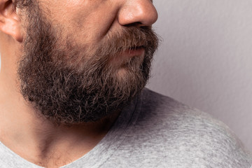 Long beard and mustache of handsome bearded man, portrait of bearded man in gray t-shirt against gray wall.