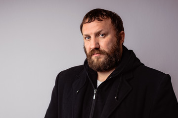 Fototapeta premium Fashion portrait handsome elegant bearded man wearing black coat against gray background wall.