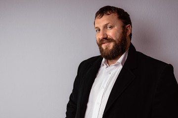 Handsome confident mature man with beard who wearing coat and shirt stands on gray background.