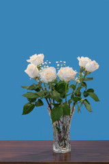 bouquet of white roses with green leaves and small white flowers, in a glass vase