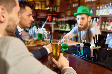 Handsome young businessmen wearing classical suits drinking beer and chatting with bearded barman while taking rest in pub after hard working day