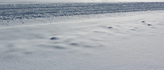 Automobile tire tread marks on a snowy winter road and a sidewalk completely covered by snow