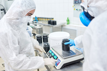 Profile view of concentrated factory worker wearing overall and safety mask using electronic scale...