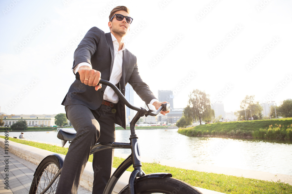 Wall mural businessman riding bicycle to work on urban street in morning.