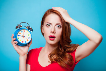 Young beautfiul redhead girl with alarm clock on blue background © Masson
