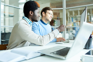 Multi-ethnic group of financial managers gathered together in front of computer and preparing annual accounts, interior of boardroom with glass walls on background