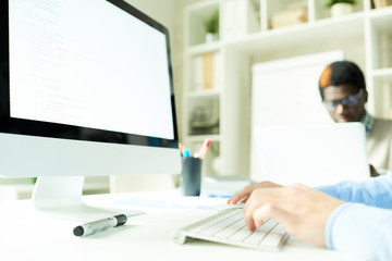 Fototapeta premium Close-up shot of unrecognizable manager sitting at desk and using computer with blank screen, interior of spacious open plan office on background