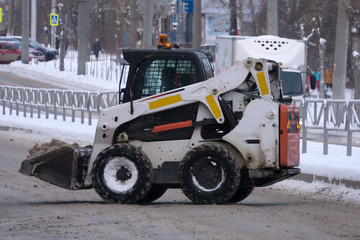 Small tractor loader machine clean and load snow and ice into a truck from a city streets after heavy snowfall .